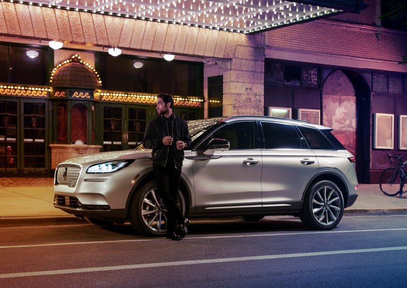 A 2022 Lincoln Corsair SUV is parked outside a theater as the driver relaxes against the frame and lights illuminate the floating roofline and body | Randy Marion Lincoln in Statesville NC