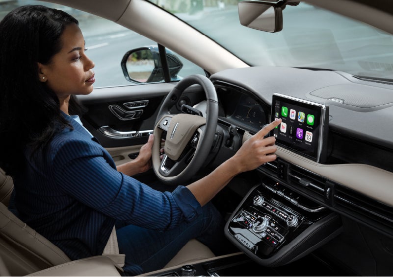 A woman in the driver's seat of a 2022 Lincoln Corsair is touching the center digital screen to connect to Apple CarPlay® | Randy Marion Lincoln in Statesville NC