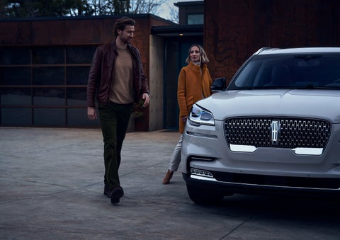 A man and a woman approaching a 2024 Lincoln Aviator® SUV, which illuminates certain lights when they are close | Randy Marion Lincoln in Statesville NC