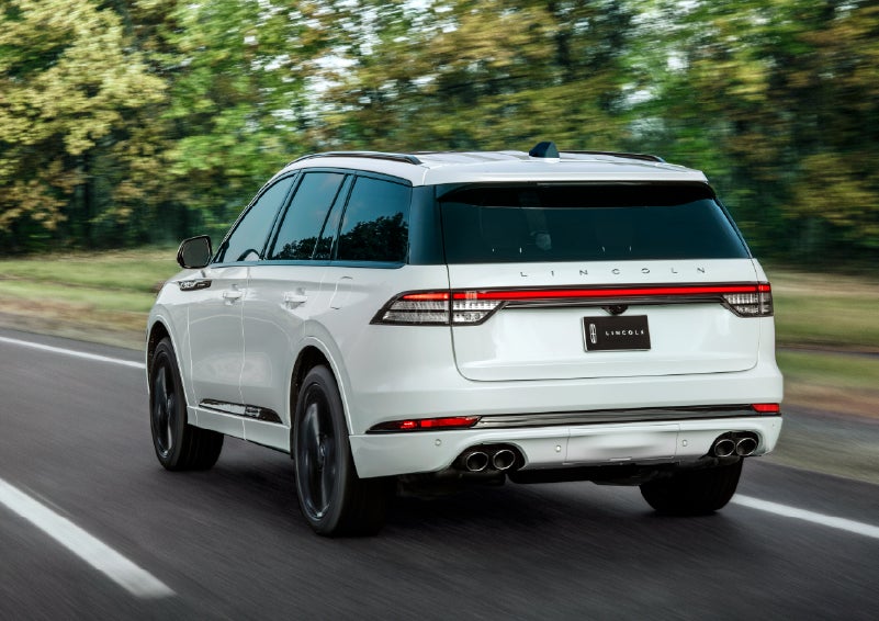 A white 2026 Lincoln Aviator® SUV is being driven away down a road lined with colorful trees. | Randy Marion Lincoln in Statesville NC