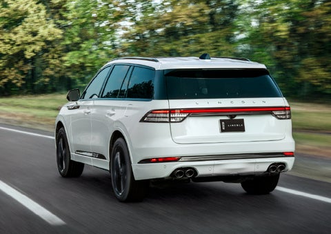 A white 2026 Lincoln Aviator® SUV is being driven away down a road lined with colorful trees. | Randy Marion Lincoln in Statesville NC